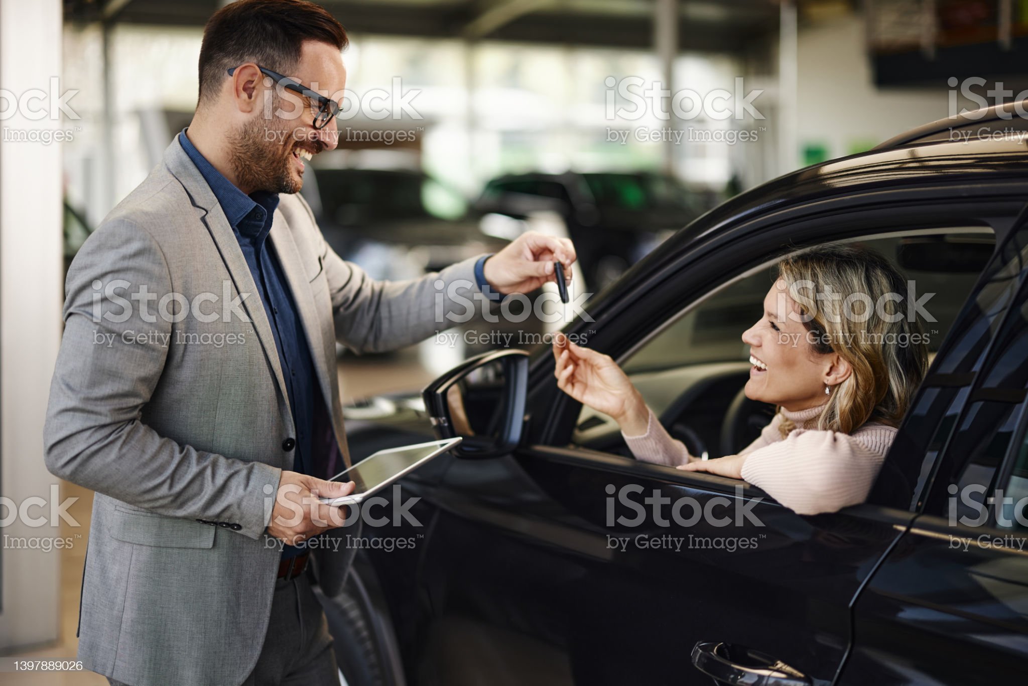 Happy woman receiving car keys from salesman in a showroom.